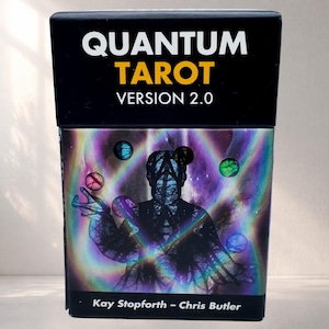 May include: A black box with the words "QUANTUM TAROT VERSION 2.0" in white and yellow. The box features a holographic image of a figure juggling orbs. The text "Kay Stopforth - Chris Butler" is at the bottom.