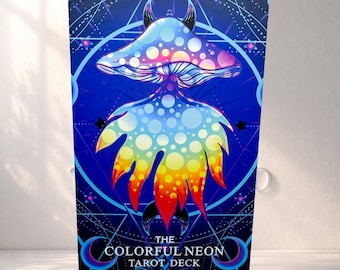 May include: A tarot deck box with a colourful mushroom illustration in blue, pink, yellow, and orange. The text "THE COLORFUL NEON TAROT DECK" is at the bottom. The background features geometric shapes and stars, creating a cosmic theme.