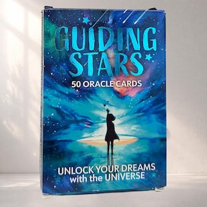 Puede incluir: Un juego de cartas de oráculo "Guiding Stars". La caja presenta un diseño de cielo estrellado con las palabras "Guiding Stars" en una fuente azul brillante. La caja también incluye el texto "50 Cartas de Oráculo" y "Unlock Your Dreams with the Universe."