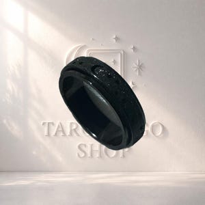 May include: A black ring with a textured surface. The ring has a spinning band and is set against a white background with the text "TAROT GO SHOP".