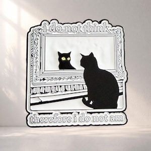 May include: A black and white enamel pin featuring a black cat sitting before a framed mirror. The cat's reflection shows yellow eyes. The text "I DO NOT THINK" appears at the top, and "therefore i do not am" is printed at the bottom.