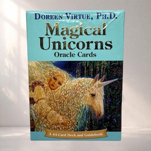 May include: A teal box of "Magical Unicorns Oracle Cards" by Doreen Virtue, Ph.D. The box features a golden unicorn with a woman's face and long blonde hair. The text "A 44-Card Deck and Guidebook" is at the bottom.