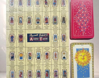 May include: Astro-Tarot deck featuring a grid of card images with text, a red deck with a star and moon pattern, and a single card with a sun illustration. The deck is labeled "Russell Grant's Astro-Tarot".