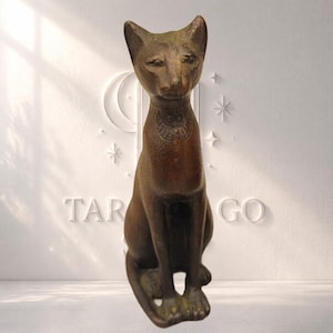 Puede incluir: Una estatua de gato de color bronce en posición sentada. El gato tiene orejas puntiagudas, una cara detallada y un collar. La estatua está sobre un fondo blanco con las palabras "TAR" y "GO" visibles.
