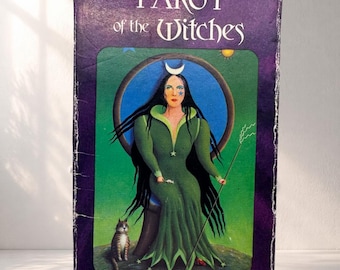 May include: A vintage Tarot of the Witches card deck box. The box is purple with the title in white script. The front features a green illustration of a witch with long black hair, a crescent moon, and a cat. The witch is holding a staff.