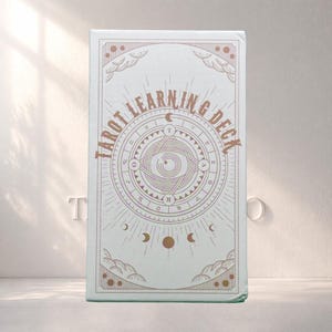 Könnte beinhalten: Hellblaue Tarotkarten-Deckbox mit dem Text "Tarot Learning Deck" in einem kreisförmigen Design. Das Design umfasst goldfarbene Monde, Sterne und geometrische Muster. Das Deck ist zum Erlernen des Tarot gedacht.