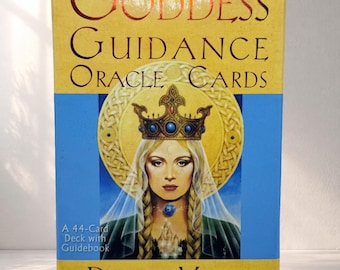 May include: A rectangular box for "Goddess Guidance Oracle Cards" by Doreen Virtue. The box features a portrait of a woman wearing a crown and a blue gemstone necklace, set against a blue and gold background. The text "A 44-Card Deck with Guidebook" is also visible.