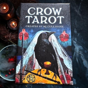 May include: A tarot deck titled "CROW TAROT" with a black crow illustration. The deck cover features the text "CREATED BY MJ CULLINANE" and a background with a starry sky and pomegranate illustrations. The crow is perched on a yellow surface.