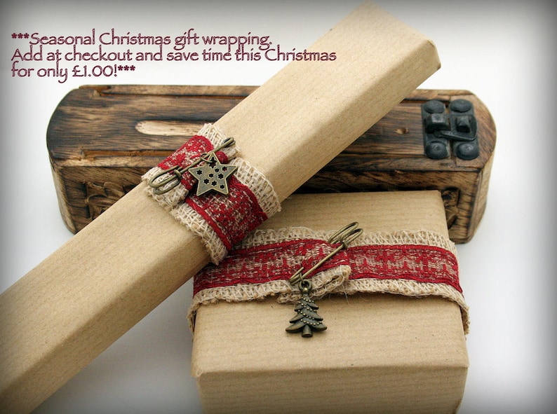 May include: Two brown gift boxes wrapped in brown paper with red and beige ribbon and a star and a Christmas tree charm. The text on the top box reads "***Seasonal Christmas gift wrapping. Add at checkout and save time this Christmas for only &pound;1.00!***"