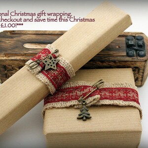 Puede incluir: Dos cajas de regalo marrones envueltas en papel marr&oacute;n con cinta roja y beige y un amuleto de estrella y &aacute;rbol de Navidad. El texto en la caja superior dice "***Envoltorio de regalo de Navidad de temporada. Agrega en la caja y ahorra tiempo esta Navidad por solo &pound; 1.00!***"