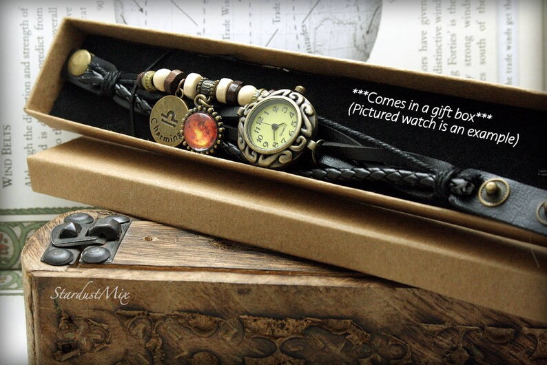 Puede incluir: Un brazalete de reloj de cuero negro con una esfera de reloj dorada y un dije con el s&iacute;mbolo astrol&oacute;gico de Piscis. El brazalete est&aacute; en una caja de regalo marr&oacute;n.