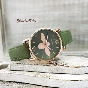 May include: A green leather wristwatch with a rose gold case and a bee design on the face. The watch face has Roman numeral hour markers and the text "Bao-Diga" at the 6 o'clock position.