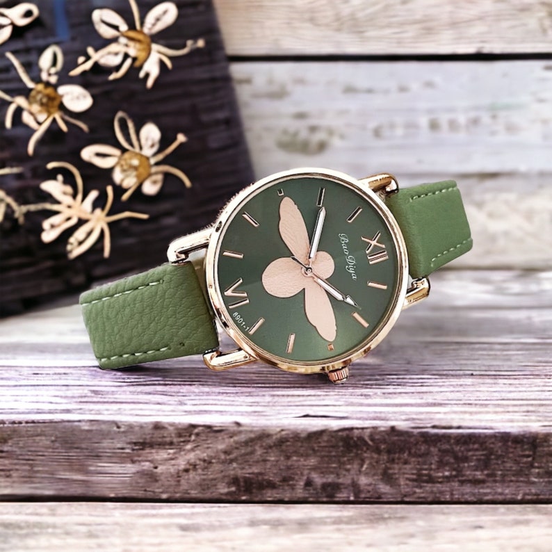 May include: A green leather wristwatch with a gold-tone case and a bee design on the face. The watch face has Roman numeral hour markers and the text "Bao Diya" at the 6 o'clock position.