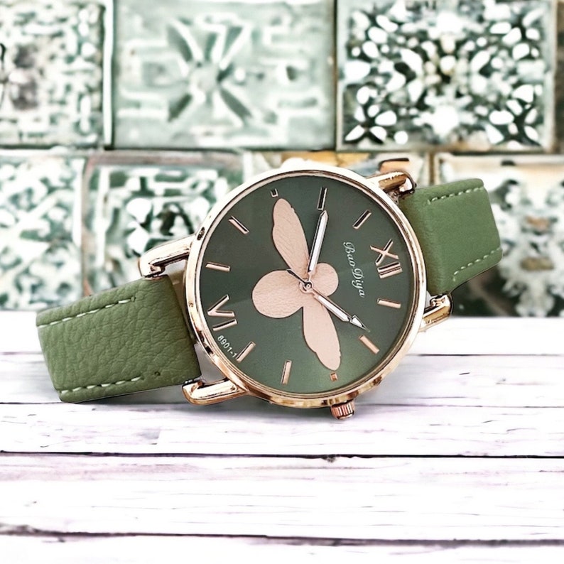 May include: A green leather wristwatch with a gold-tone case and a bee design on the face. The watch face has Roman numeral hour markers and the text "Bao Diya" printed on it.