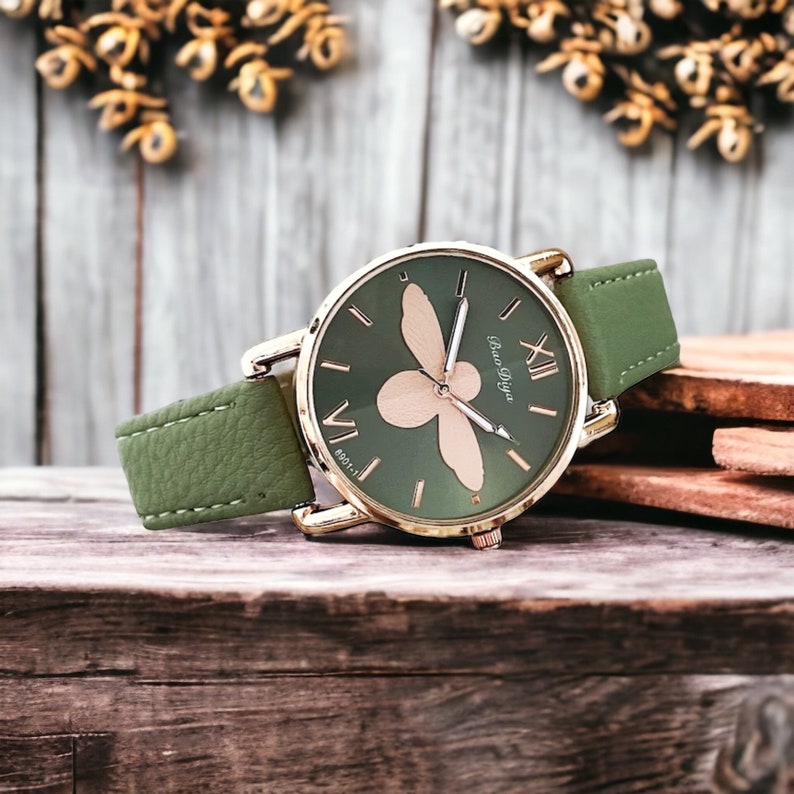 May include: A green leather wristwatch with a gold-tone case and a bee design on the face. The watch face has Roman numeral hour markers and the text "Bao Diya" at the 6 o'clock position.