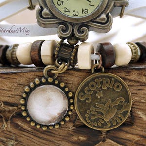 Puede incluir: Un brazalete de reloj de cuero blanco con cuentas de madera marr&oacute;n y dos dijes de bronce. Un dije es un disco redondo, en blanco y el otro es un dije redondo con la palabra "Scorpio" y un dise&ntilde;o de escorpi&oacute;n.