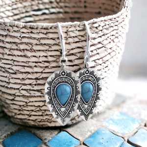 Puede incluir: Un par de pendientes colgantes de plata con piedras turquesa azules engastadas en un diseño decorativo y ornamentado.