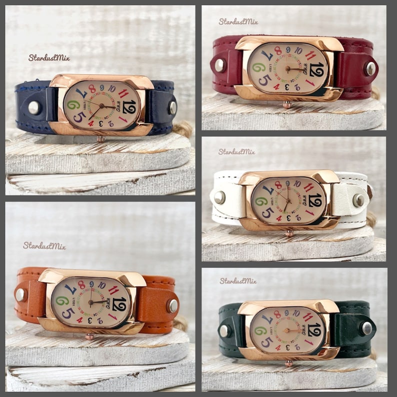 May include: Four different coloured leather wristwatches with rose gold cases and colourful numbers on the face. The watches are on a white wooden background.