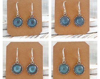 May include: Pair of silver dangle earrings with blue and green mandala designs on the round pendant. The earrings are displayed on a brown card with the text "Stardustmix" printed on it.