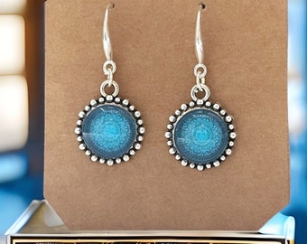 May include: Silver dangle earrings with a blue and gray mandala design. The earrings have a beaded border.
