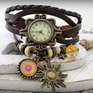 May include: A brown leather watch with a square face and a sun and mandala charm. The watch has a braided leather band and is decorated with wooden beads and a clear amber bead.