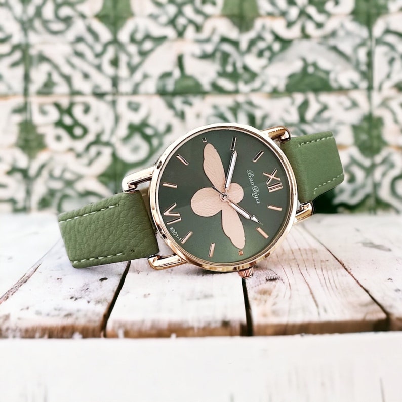 May include: A green leather wristwatch with a gold-tone case and a bee design on the face. The watch face has Roman numeral hour markers and the text "Bao Diya" printed on it.