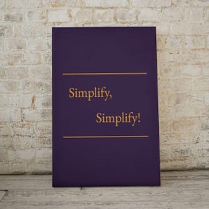 Puede incluir: Un lienzo rectangular con un fondo morado oscuro. Las palabras "Simplify, Simplify!" están escritas en oro, con una línea dorada encima y debajo del texto. El lienzo se muestra contra una pared de ladrillos.