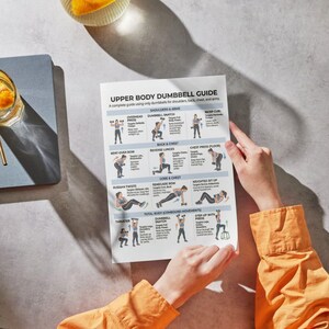 May include: A person holding a printed "Upper Body Dumbbell Guide" with exercise illustrations. The guide includes exercises for shoulders, back, chest, and arms. The person is wearing an orange long-sleeved shirt. A drink with a straw is visible in the background.