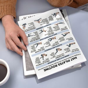 May include: A person's hand holding a printed Pilates routine guide. The guide features illustrated exercises for core strength, flexibility, and muscle tone. The routine includes exercises like the Hundred, Pelvic Tilt, and Single Leg Stretch.