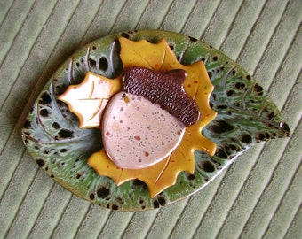 May include: A ceramic leaf dish with a brown and tan acorn design. The dish is green with brown speckles.