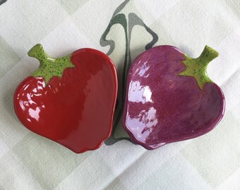 May include: Two ceramic strawberry-shaped dishes, one red and one purple, with green leaves.