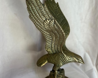 May include: A brass eagle sculpture with outstretched wings. The eagle is perched on a globe-shaped base atop a circular platform. The sculpture has detailed feathering and a polished finish, showcasing a classic design.