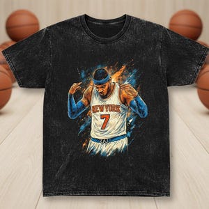Puede incluir: Camiseta negra con una ilustración estilizada de un jugador de baloncesto con una camiseta de Nueva York con el número 7. El diseño incluye detalles en azul y naranja. Balones de baloncesto en el fondo.