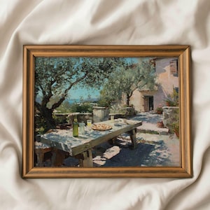 May include: A framed painting of an outdoor dining scene. A wooden table is set with food and drinks, under olive trees. The background shows a building and a sea view. The frame is a warm brown colour.