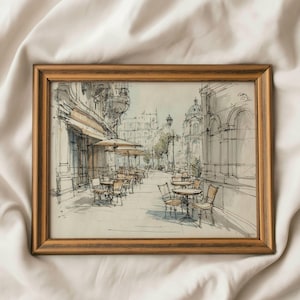 Könnte beinhalten: Gerahmte Skizze einer europäischen Straßenszene mit einem Café. Das Kunstwerk zeigt detaillierte Zeichnungen von Gebäuden, Tischen, Stühlen und Sonnenschirmen. Der Rahmen hat eine warme, hellbraune Farbe.
