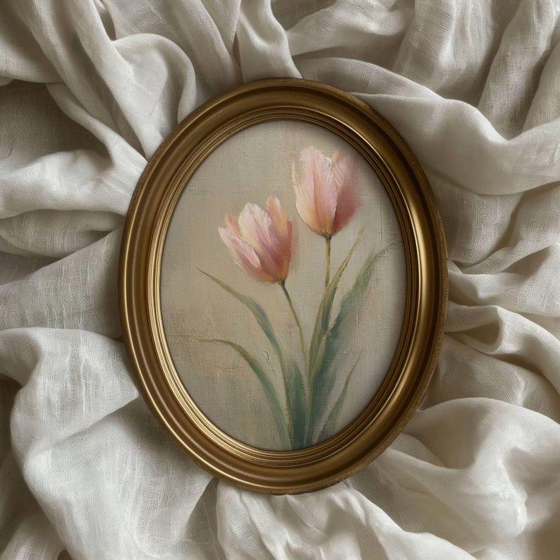 K&ouml;nnte beinhalten: Oval gerahmtes Gem&auml;lde mit zwei rosa Tulpen mit gr&uuml;nen Stielen und Bl&auml;ttern. Das Kunstwerk ist vor einem cremefarbenen Hintergrund platziert und in einem goldfarbenen ovalen Rahmen gerahmt. Das Gem&auml;lde wird auf einem wei&szlig;en, strukturierten Stoff pr&auml;sentiert.