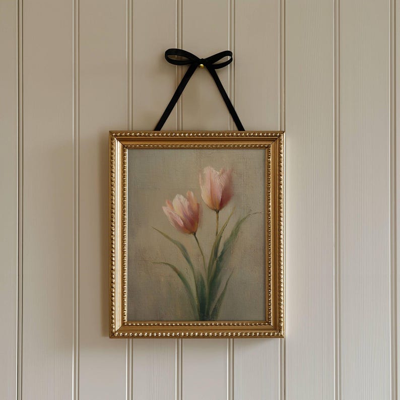 K&ouml;nnte beinhalten: Gerahmtes Gem&auml;lde mit zwei rosa Tulpen mit gr&uuml;nen Stielen und Bl&auml;ttern. Das Gem&auml;lde befindet sich in einem goldenen, verzierten Rahmen und wird von einem schwarzen Band gehalten, das zu einer Schleife gebunden ist.