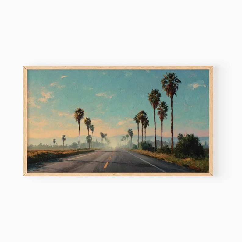 May include: A framed landscape painting depicts a road lined with tall palm trees under a blue sky with wispy clouds. The road stretches into the distance, with a hazy atmosphere in the background. The artwork has a warm, inviting color palette.