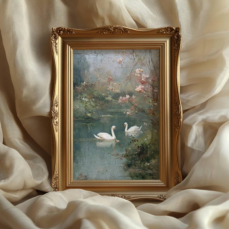 May include: A framed painting featuring two white swans on a tranquil lake, surrounded by lush greenery and delicate pink blossoms. The artwork is set within an ornate gold frame, creating a classic and elegant aesthetic.