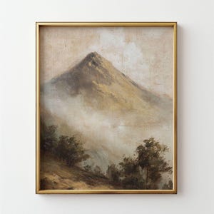 May include: A framed landscape painting depicting a mountain peak rising through the clouds. The artwork uses a muted palette of browns, tans, and whites, with a gold frame. Trees are visible in the foreground of the painting.