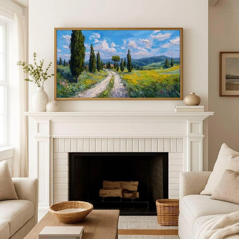 May include: A framed landscape painting depicts a winding dirt road through a field of yellow flowers and tall green trees under a blue sky with fluffy white clouds. The painting is displayed above a white fireplace.