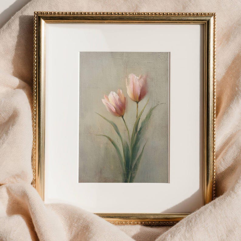 K&ouml;nnte beinhalten: Ein gerahmter Kunstdruck mit zwei rosa Tulpen mit gr&uuml;nen Stielen und Bl&auml;ttern vor einem ged&auml;mpften Hintergrund. Das Kunstwerk ist in einem goldfarbenen, verzierten Rahmen eingefasst, der dem botanischen Thema eine elegante Note verleiht.