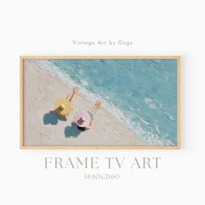 May include: A framed painting depicts a beach scene with two figures sunbathing, wearing hats. The artwork features a light blue ocean, sandy beach, and a wooden frame. Text on the image reads "Vintage Art by Özge" and "FRAME TV ART 3840x2160".