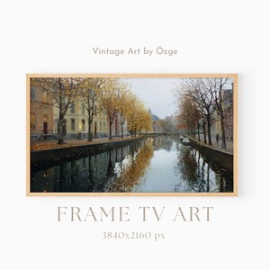May include: A digital landscape painting of a canal lined with yellow autumn trees and buildings, framed in light wood. The text reads: Vintage Art by Özge, FRAME TV ART, 3840x2160 px. The scene features reflections on the water surface.
