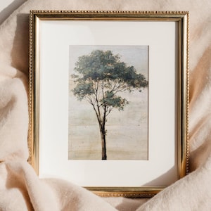 May include: A framed art print featuring a tree with green foliage and a brown trunk. The artwork is set against a neutral background and framed in a gold-colored, ornate frame. The frame is rectangular with a white mat.