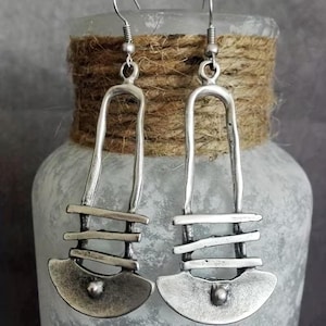 May include: A pair of silver-toned dangle earrings featuring a long, open-arched frame with three horizontal bars and a curved, semi-circular base. Each earring includes a small, centered spherical accent at the bottom and a standard hook wire.