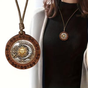 May include: A brown pendant necklace featuring a sun and moon design. The pendant is circular with a detailed celestial illustration in gold, silver, and brown tones. The necklace has a brown cord.