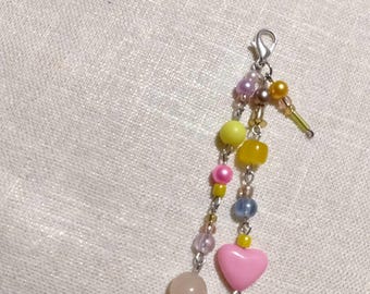 May include: A beaded charm with a silver clasp. The charm features a variety of colorful beads, including yellow, pink, purple, and clear beads. A pink heart-shaped bead and a round, light pink bead are also included.