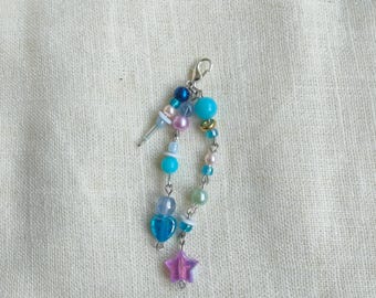 May include: A beaded charm with a silver clasp. The charm features a variety of beads in shades of blue, pink, and iridescent colors, including round beads, heart-shaped beads, and a star-shaped charm. The charm is attached to a silver earring post.