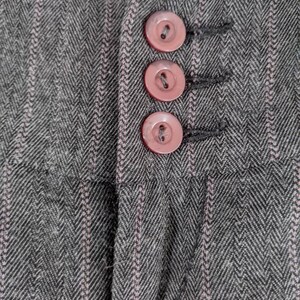 Peut inclure: Gros plan sur un tissu gris &agrave; chevrons avec des rayures roses verticales. Trois boutons roses sont visibles, cousus sur le tissu. Les boutons sont ronds et ont un bord l&eacute;g&egrave;rement sur&eacute;lev&eacute;. Le tissu semble &ecirc;tre une mati&egrave;re tiss&eacute;e.